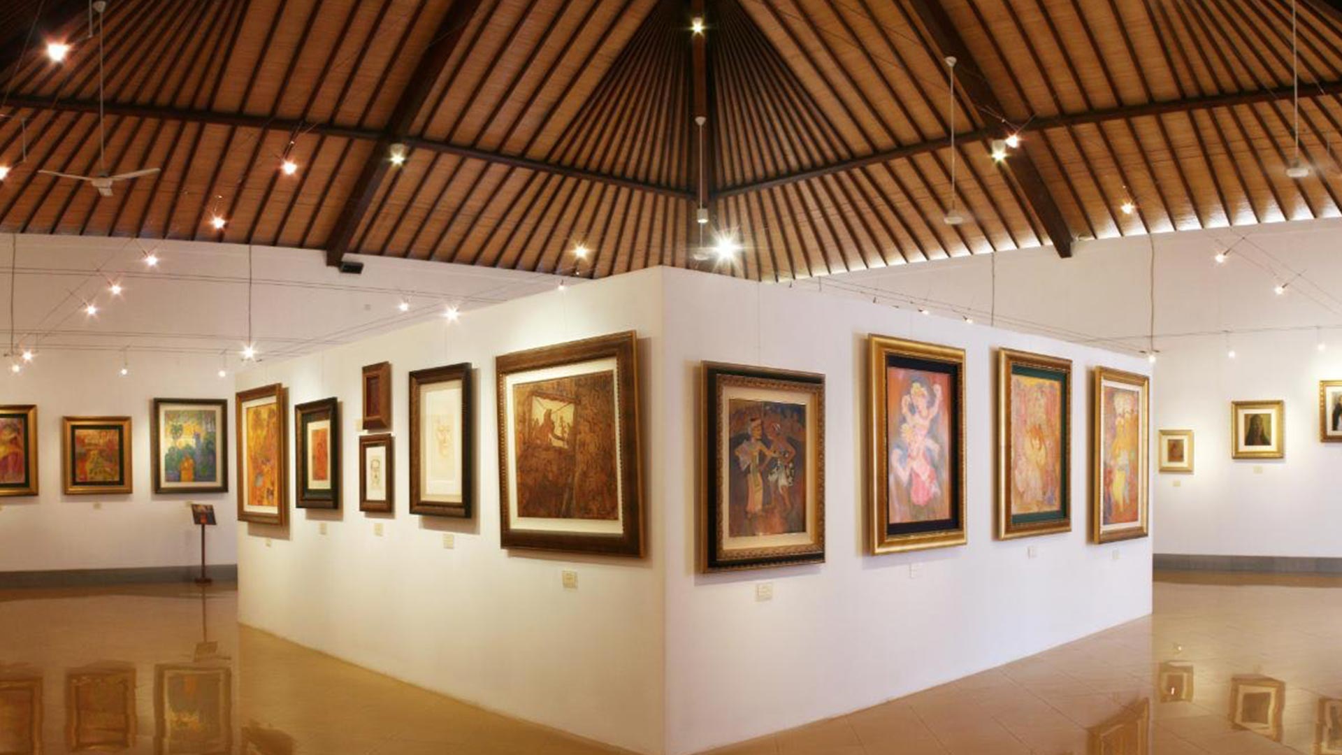 Interior of Museum Pasifika Nusa Dua with framed paintings on white walls under a high wooden ceiling