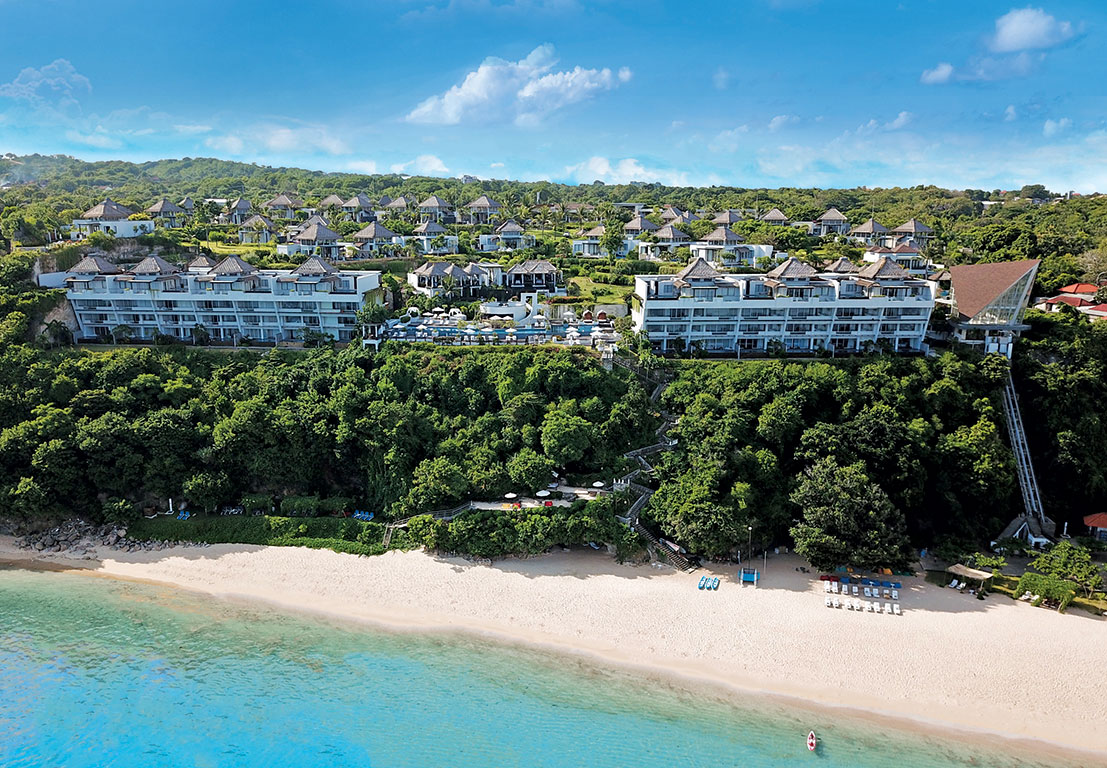 Samabe Bali Suites and Villas perched on a green cliff above a white sand beach in Nusa Dua