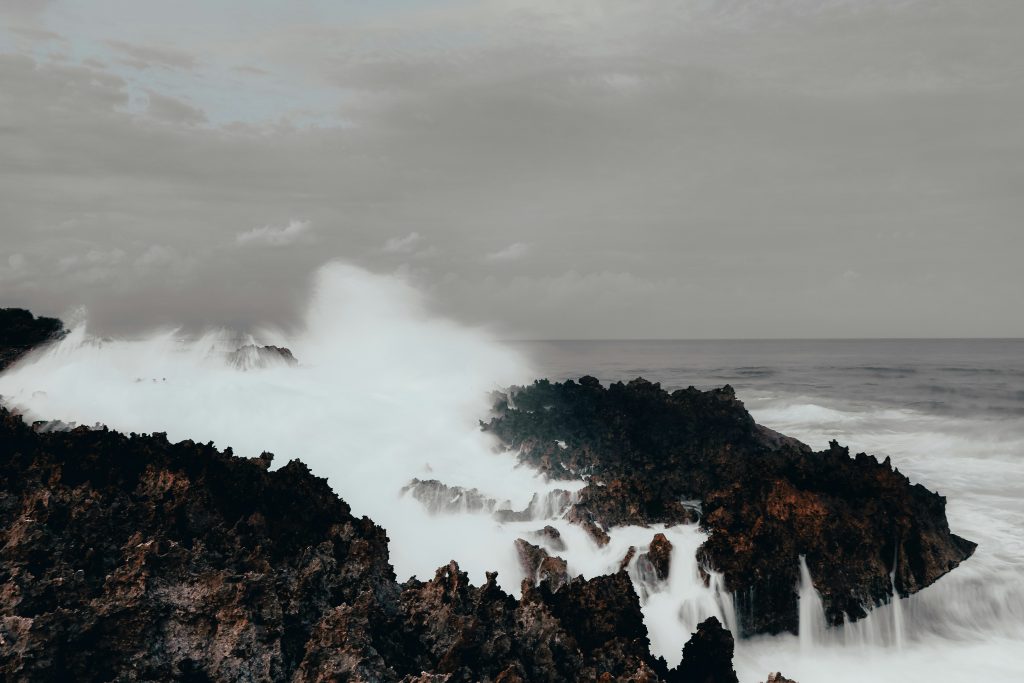 Large waves crashing against dark volcanic rocks at Waterblow Nusa Dua Bali under a cloudy sky