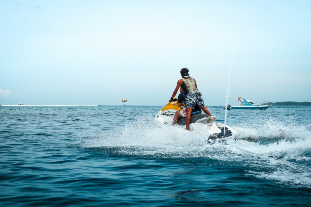 Man riding a jet ski on the open sea at Tanjung Benoa Bali with boats in the distance and water spray around him