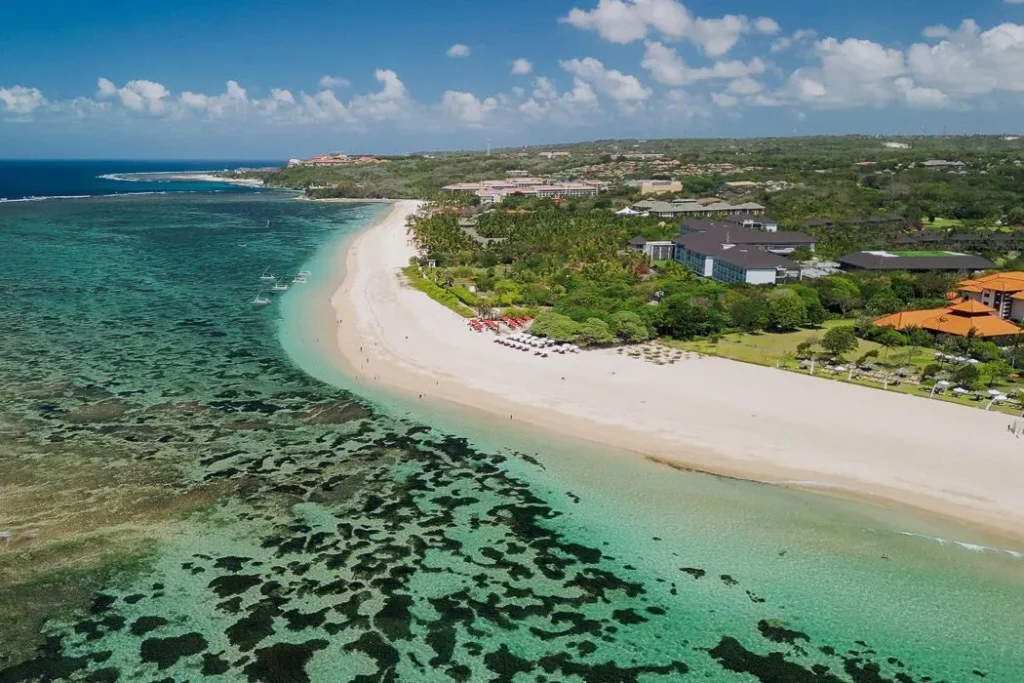 Aerial view of Mengiat Beach in Nusa Dua Bali with long white sand shoreline clear turquoise water coral reef and nearby resorts